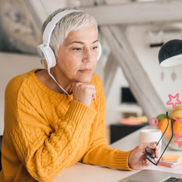 Frau in orangem Pullover sitzt vor dem Laptop und trägt Kopfhörer