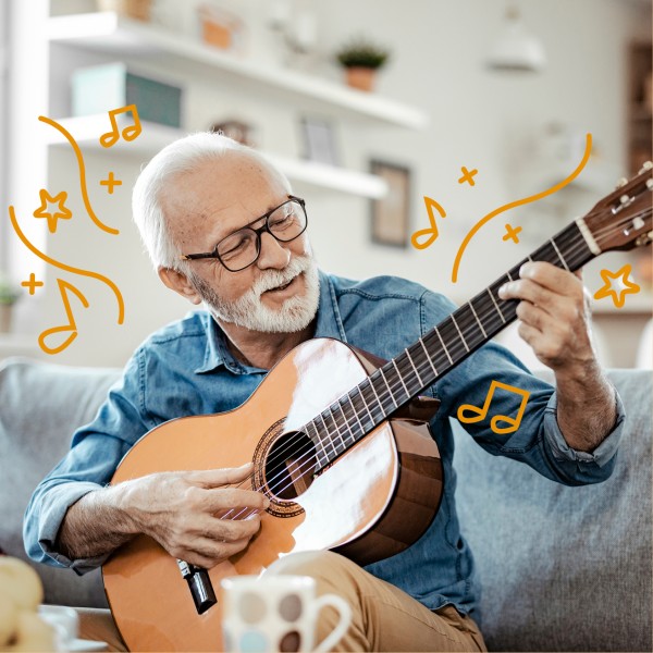 Älterer Mann mit Brille spielt Gitarre auf dem Sofa.