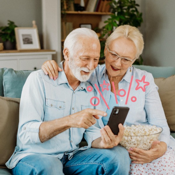 Älteres Paar sitzt auf Sofa und hält ein Handy in der Hand