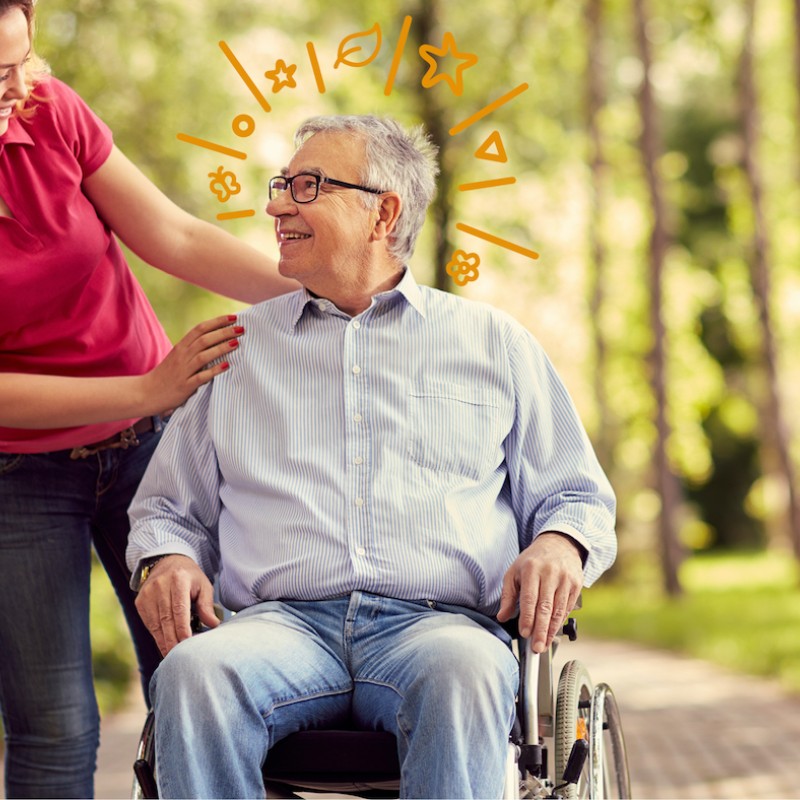 Frau schiebt Mann im Rollstuhl durch den Wald.